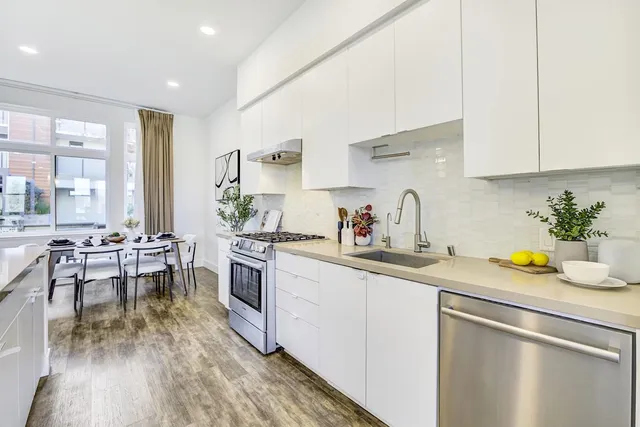 a kitchen with a sink dishwasher a stove and white cabinets with wooden floor