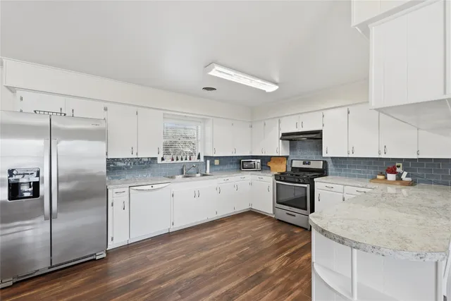 a kitchen with stainless steel appliances granite countertop a refrigerator a sink dishwasher a stove top oven a refrigerator with white cabinets and wooden floor