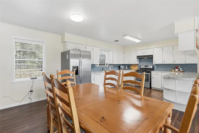 a dining room with kitchen island stainless steel appliances wooden floor dining table and chairs