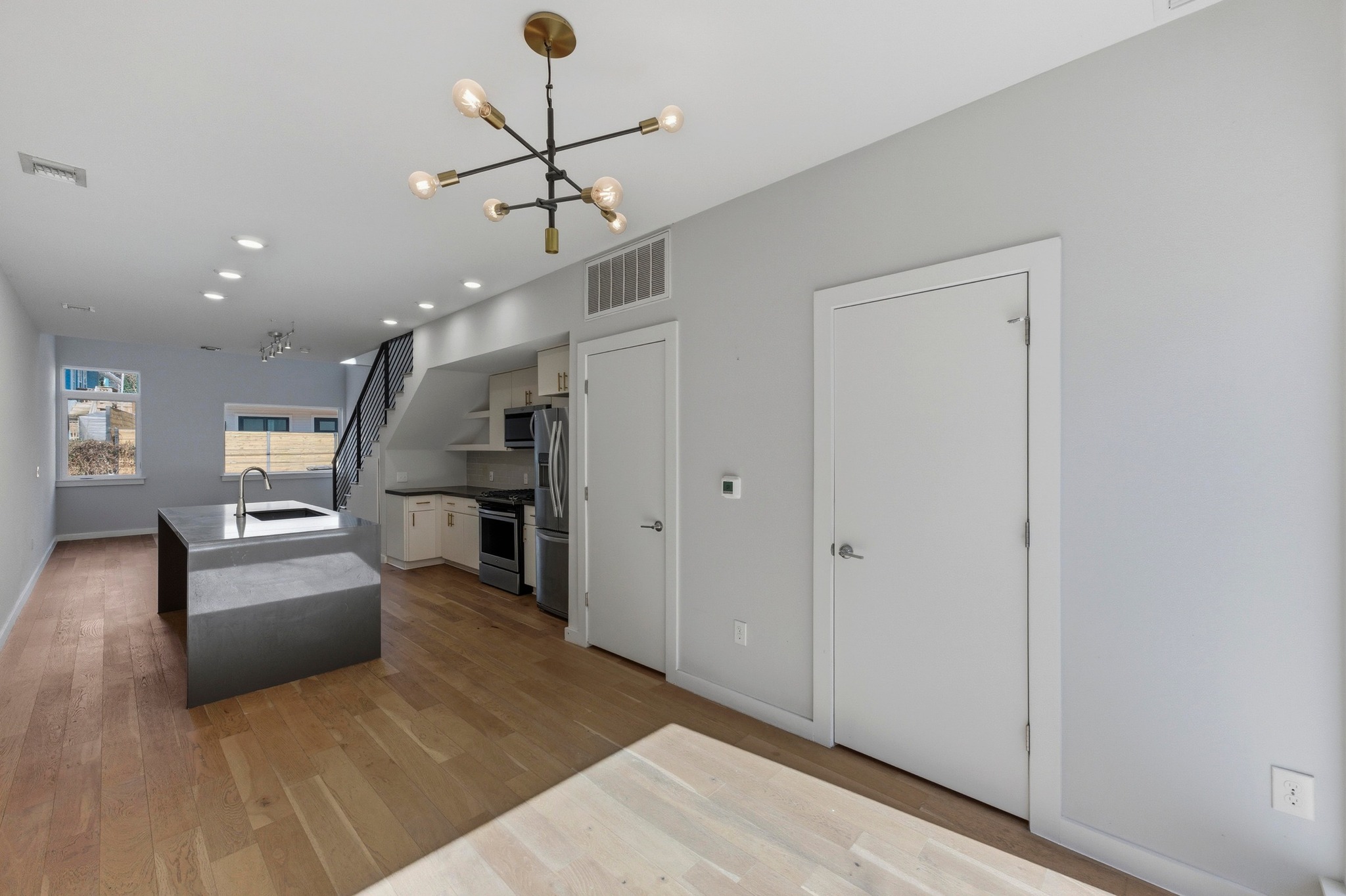 2002 East 7th Street, Unit 242 Austin, TX 78702 - Photo 14 of 34 Kitchen with an island with sink, appliances with stainless steel finishes, light wood-type flooring, a chandelier, and white cabinetry