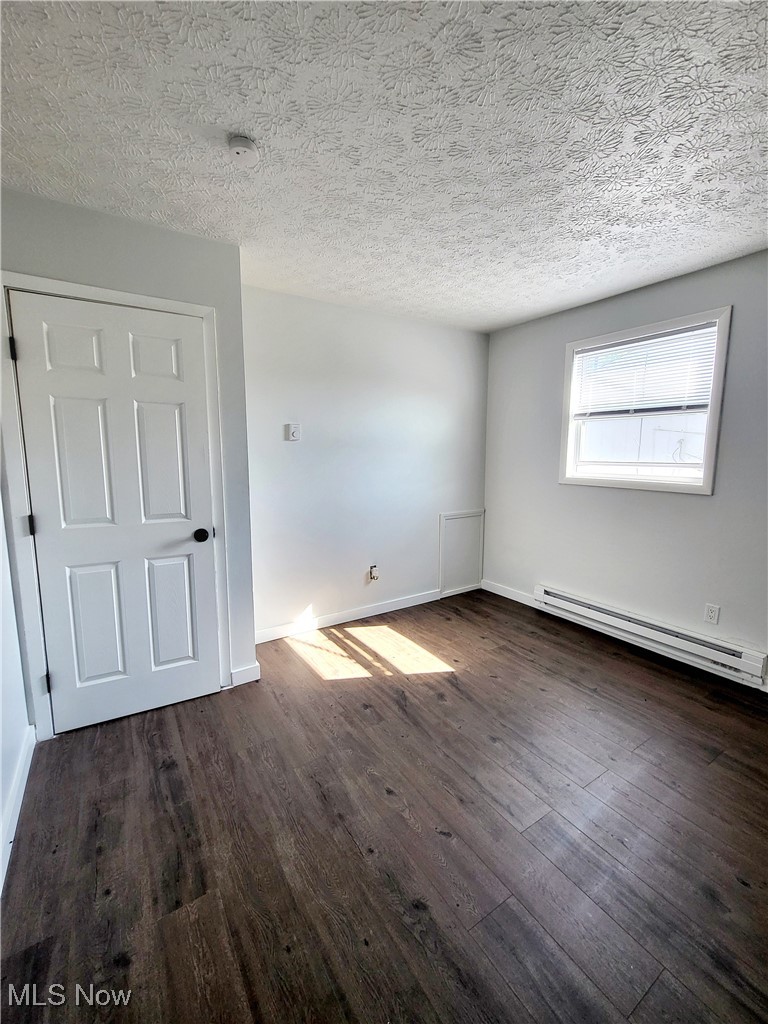 631 Root Road Lorain, OH 44052 - Photo 13 of 24 Empty room featuring a textured ceiling, dark hardwood / wood-style flooring, and a baseboard radiator