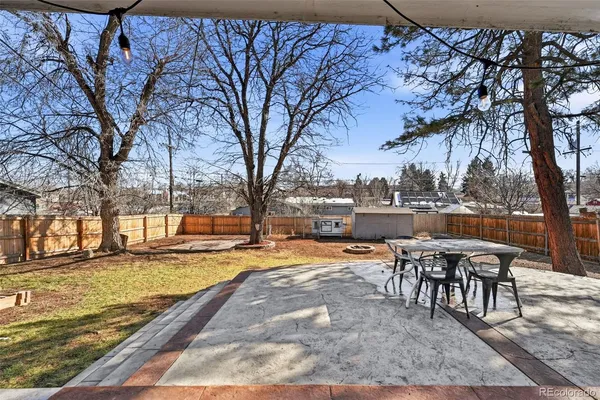 a view of a backyard with table and chairs and a barbeque with potted plants and large trees