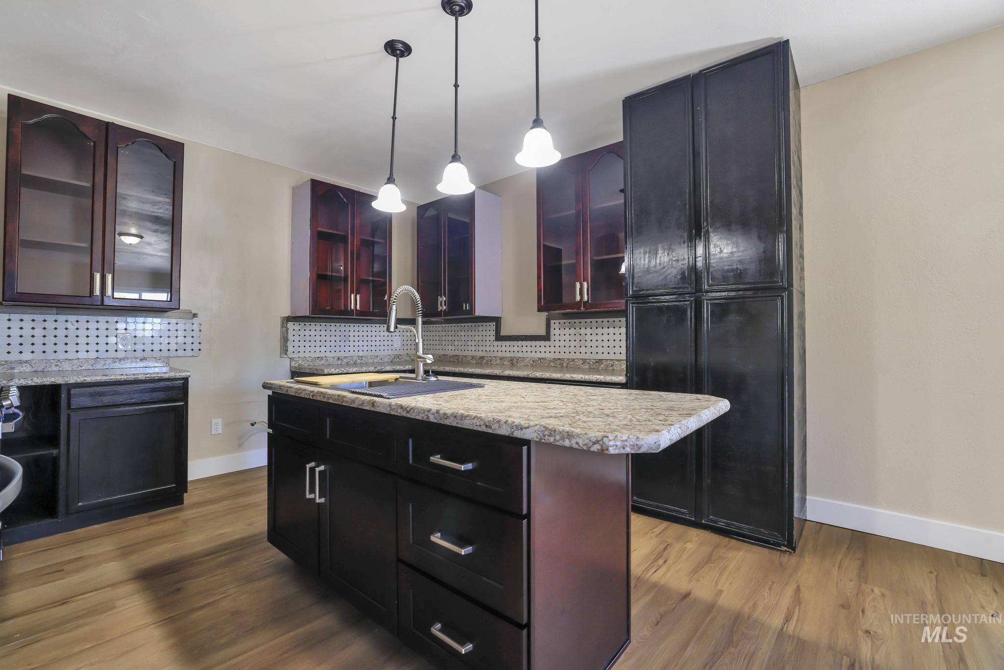 1226 Washington Street Gooding, ID 83330 - Photo 3 of 13 Kitchen with glass insert cabinets, backsplash, an island with sink, and dark wood-style flooring