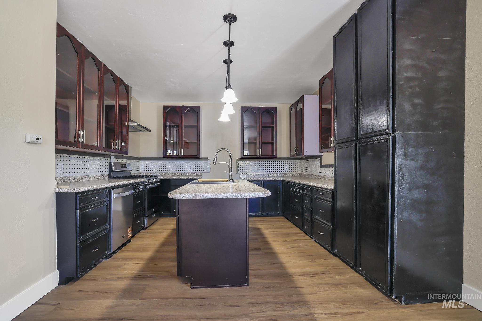 1226 Washington Street Gooding, ID 83330 - Photo 4 of 13 Kitchen with glass insert cabinets, a kitchen island with sink, hanging light fixtures, and stainless steel appliances