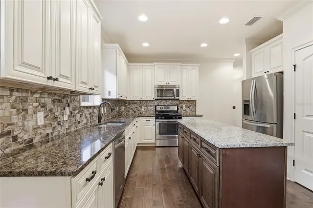 a kitchen with stainless steel appliances granite countertop a refrigerator a sink dishwasher a stove and white cabinets with wooden floor