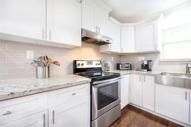 a kitchen with granite countertop stainless steel appliances a stove a sink and white cabinets