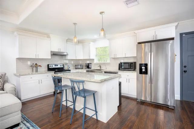 a kitchen with stainless steel appliances a stove a sink a refrigerator and white cabinets with wooden floor