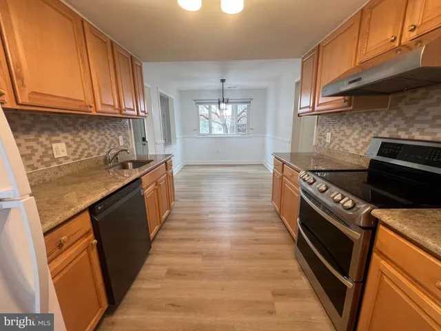 a kitchen with granite countertop a stove top oven a sink dishwasher and cabinets with wooden floor