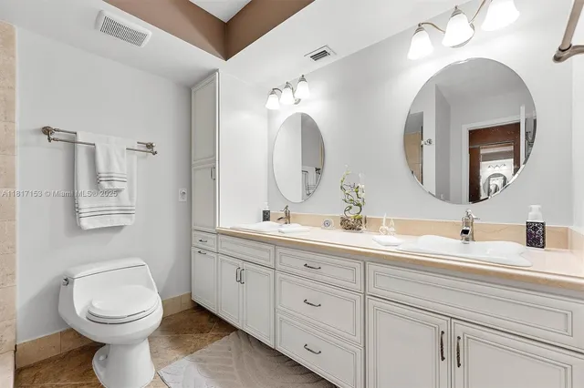 a bathroom with double vanity a toilet a double vanity and a mirror