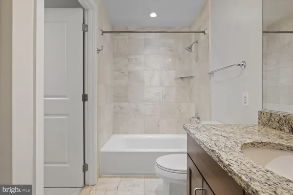 a bathroom with a granite countertop bathtub shower sink vanity and toilet