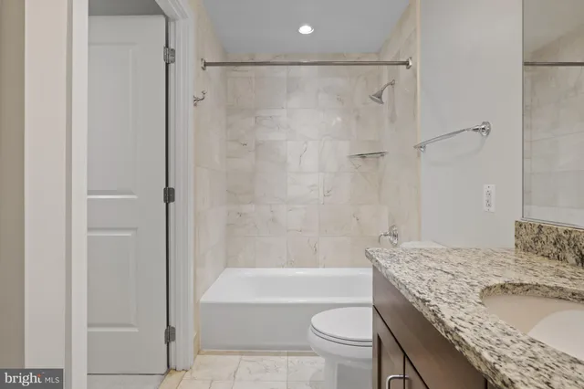 a bathroom with a granite countertop bathtub shower sink vanity and toilet