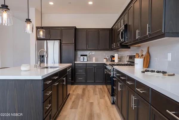 a kitchen with stainless steel appliances a sink dishwasher a stove top oven a refrigerator with wooden cabinets and floor