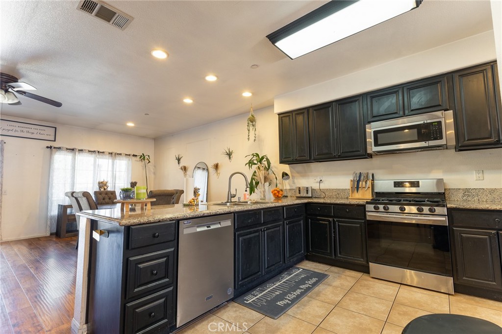 14176 Kiowa Road Apple Valley, CA 92307 - Photo 24 of 54 a kitchen with stainless steel appliances granite countertop wooden cabinets a sink dishwasher a stove and a refrigerator with wooden floor