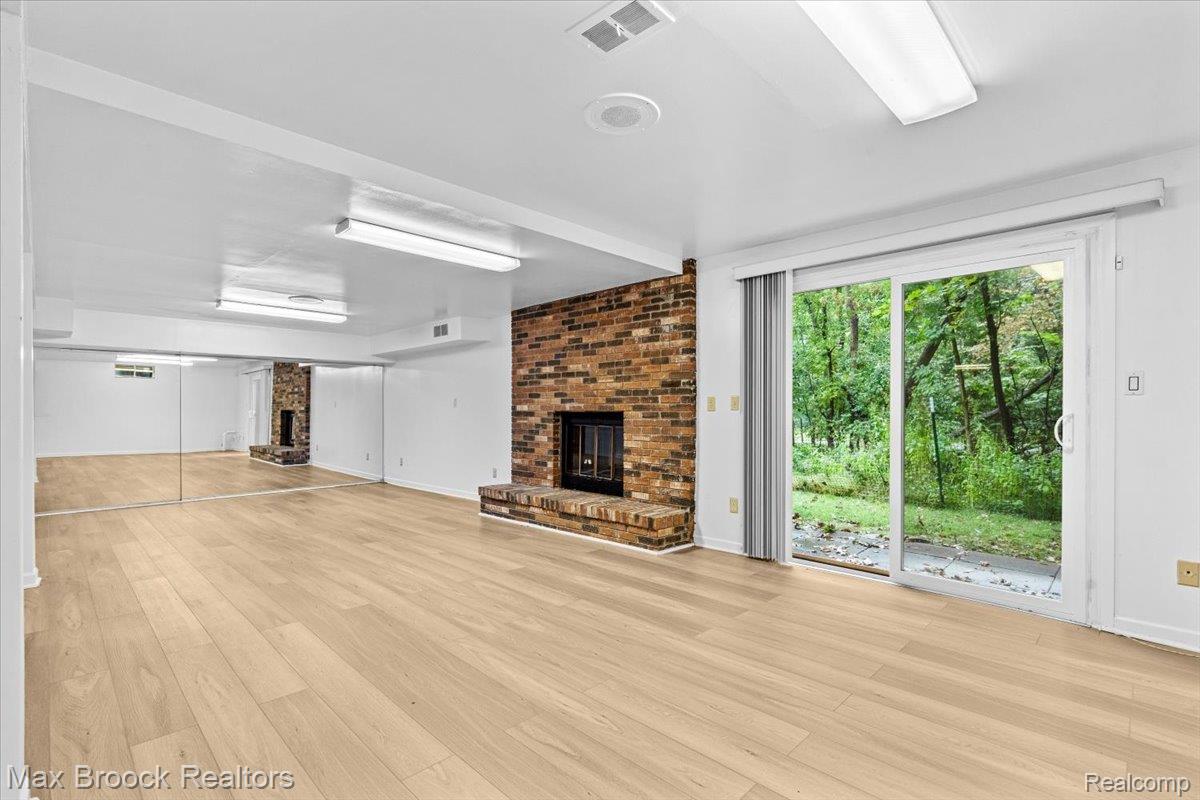 1830 Lone Pine Road Bloomfield Hills, MI 48302 - Photo 8 of 70 Spacious room featuring wood-finish flooring, a brick fireplace, full-wall mirrors, and sliding glass doors in the walkout basement with wooded privacy.
