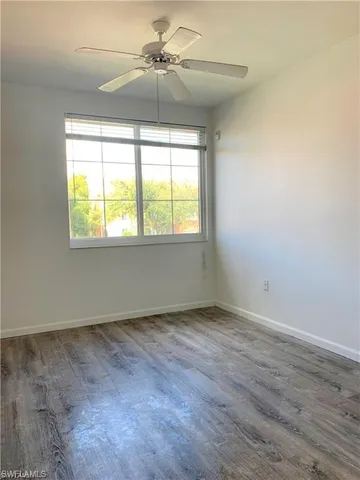 an empty room with wooden floor fan and windows