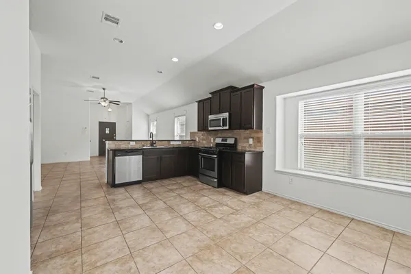 a large kitchen with kitchen island granite countertop a stove top oven a sink a counter space and cabinets