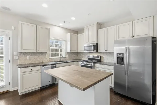 a kitchen with stainless steel appliances granite countertop a refrigerator a sink a stove a dining table and chairs