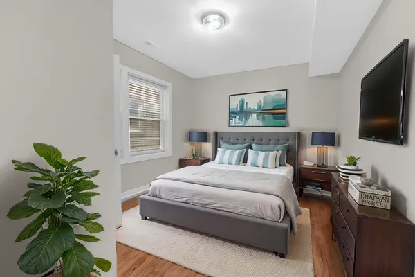 a bedroom with a bed potted plant on the dresser and a flat screen tv