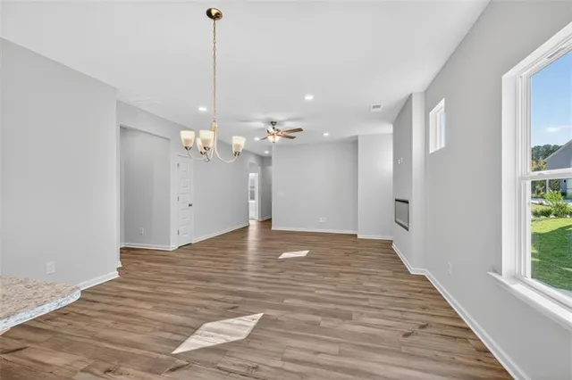 a view of an empty room with wooden floor and kitchen view