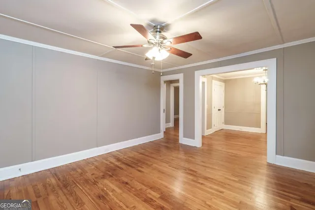 a view of an empty room with wooden floor and a ceiling fan