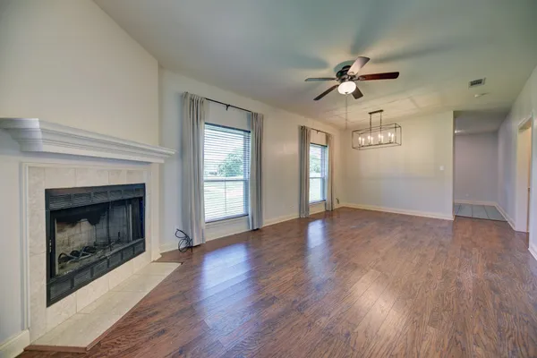 a view of an empty room with wooden floor fireplace and a window