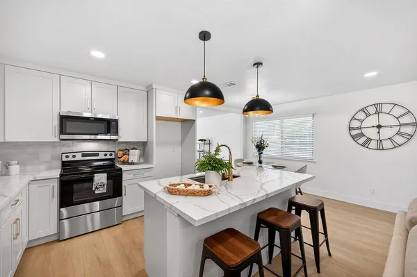 a kitchen with stainless steel appliances kitchen island granite countertop a stove a microwave a dining table and chairs with wooden floor