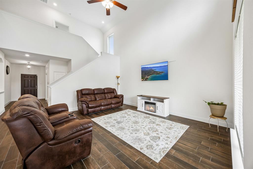 11732 Wulstone Road Fort Worth, TX 76052 - Photo 8 of 34 Vaulted living area featuring wood-finish flooring, a built-in electric fireplace, a ceiling fan with integrated lighting, and a prominent staircase