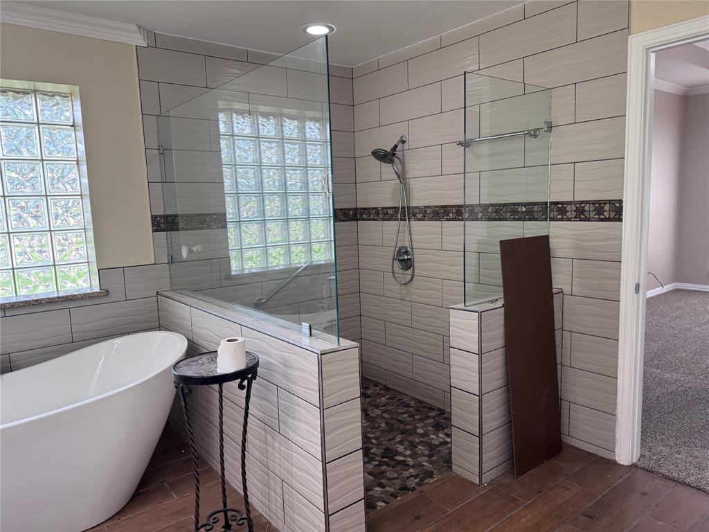1704 South Bowen Road Pantego, TX 76013 - Photo 16 of 37 Spacious bathroom featuring a freestanding soaking tub, a walk-in shower with glass panels, light-toned wall tiling, pebble-finish shower flooring, ADA compliant