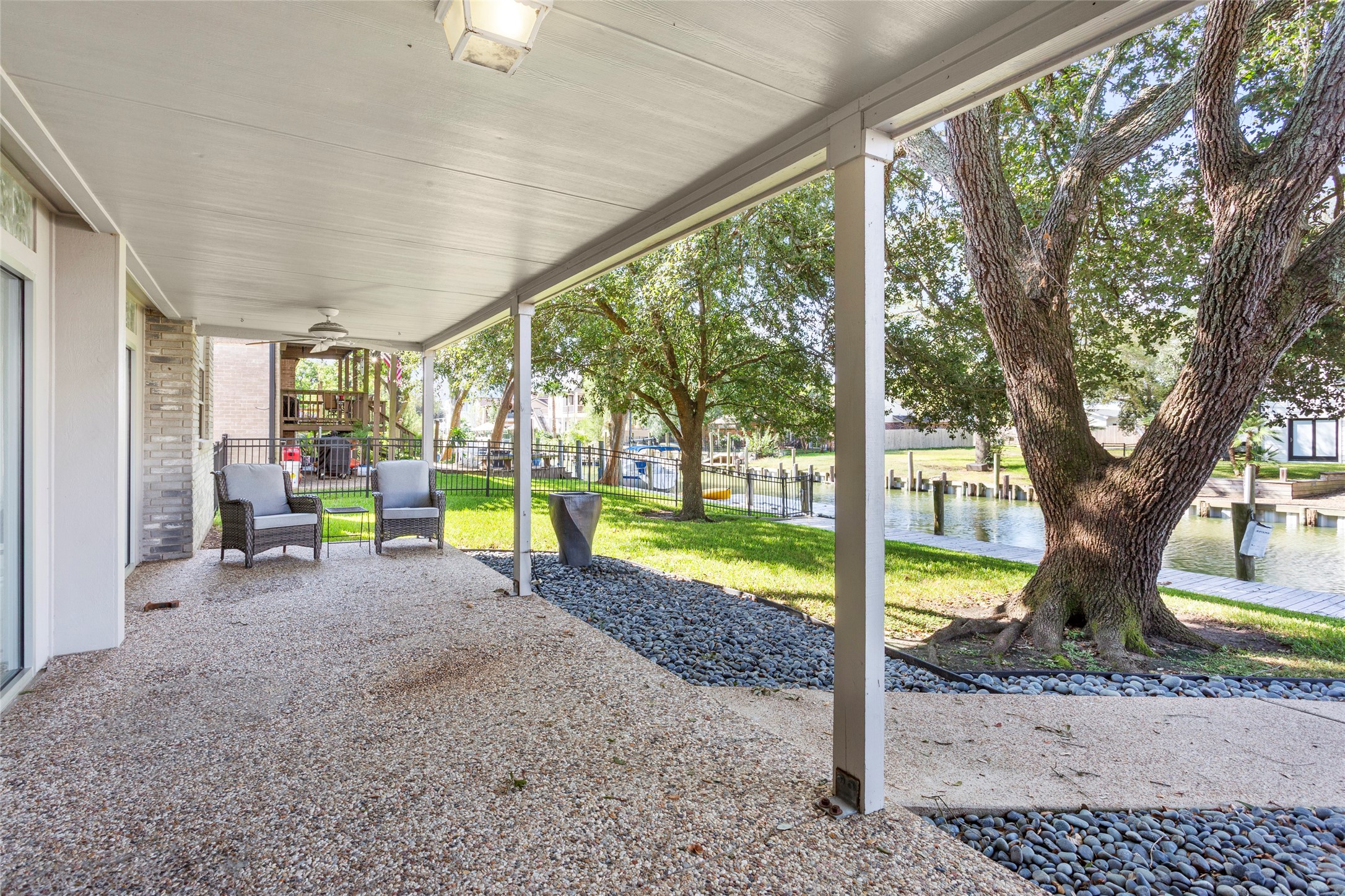 67 Harbor Lane Kemah, TX 77565 - Photo 35 of 47 This property features a spacious, lower level covered patio with seating, overlooking a serene canal. Surrounded by lush greenery and mature trees, it's perfect for outdoor relaxation and entertaining.