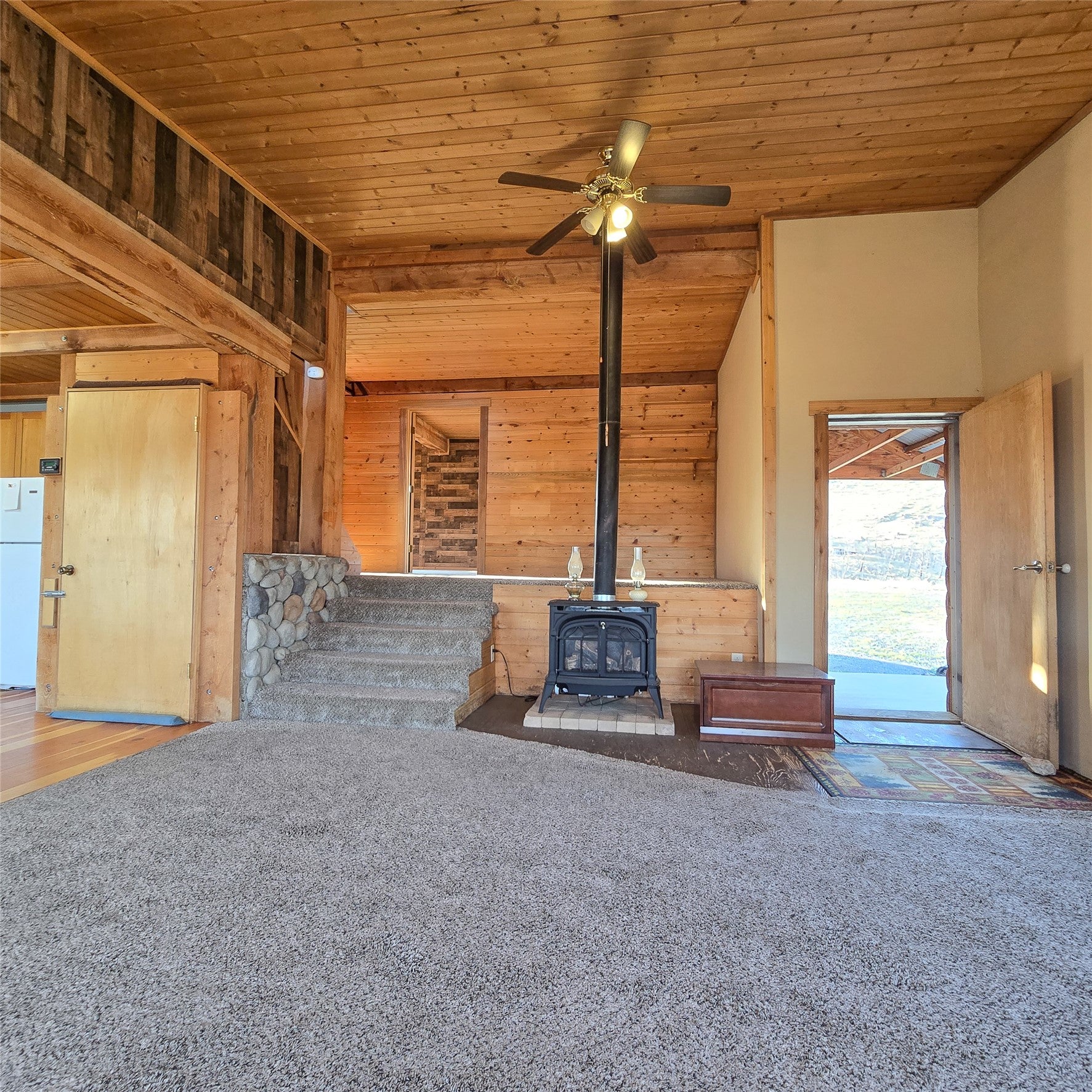 210 Friendspring Road Whitehall, MT 59759 - Photo 4 of 43 Unfurnished living room with a vaulted wood ceiling, wooden walls, carpet, a ceiling fan, and a wood stove