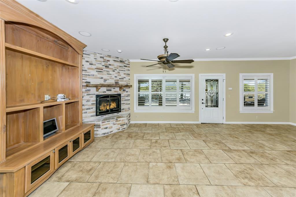 566 Selma Park Road Bowie, TX 76230 - Photo 13 of 40 Spacious living area featuring a corner fireplace with stone surround, a built-in entertainment center, tile flooring, recessed lighting, and a ceiling fan