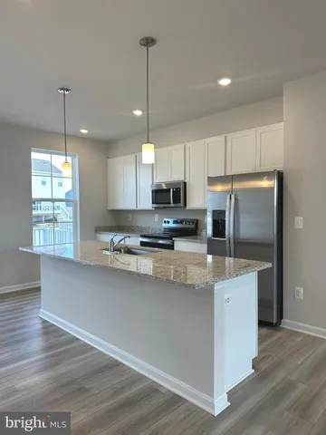 a kitchen with stainless steel appliances granite countertop a refrigerator a sink dishwasher a stove and white cabinets with wooden floor