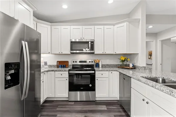 a kitchen with stainless steel appliances granite countertop a refrigerator stove a sink and white cabinets