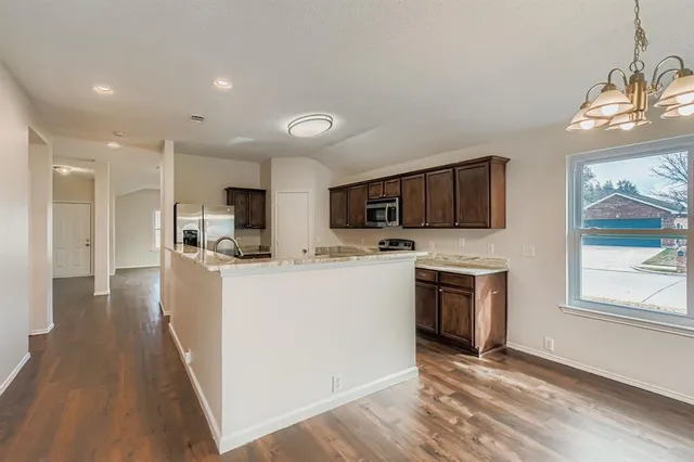 a kitchen with stainless steel appliances a stove top oven a sink a refrigerator white cabinets and wooden floor