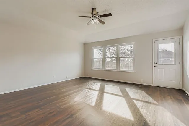 an empty room with wooden floor chandelier fan and windows