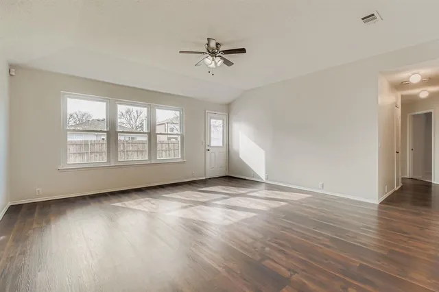an empty room with wooden floor chandelier fan and windows