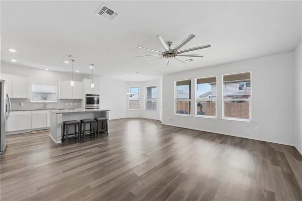 a view of an empty room with wooden floor and a kitchen