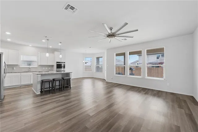 a view of an empty room with wooden floor and a kitchen