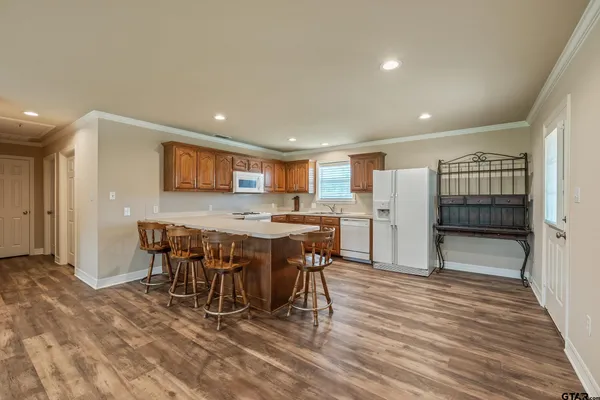 a open kitchen with stainless steel appliances kitchen island granite countertop a refrigerator a stove a dining table and chairs with wooden floor