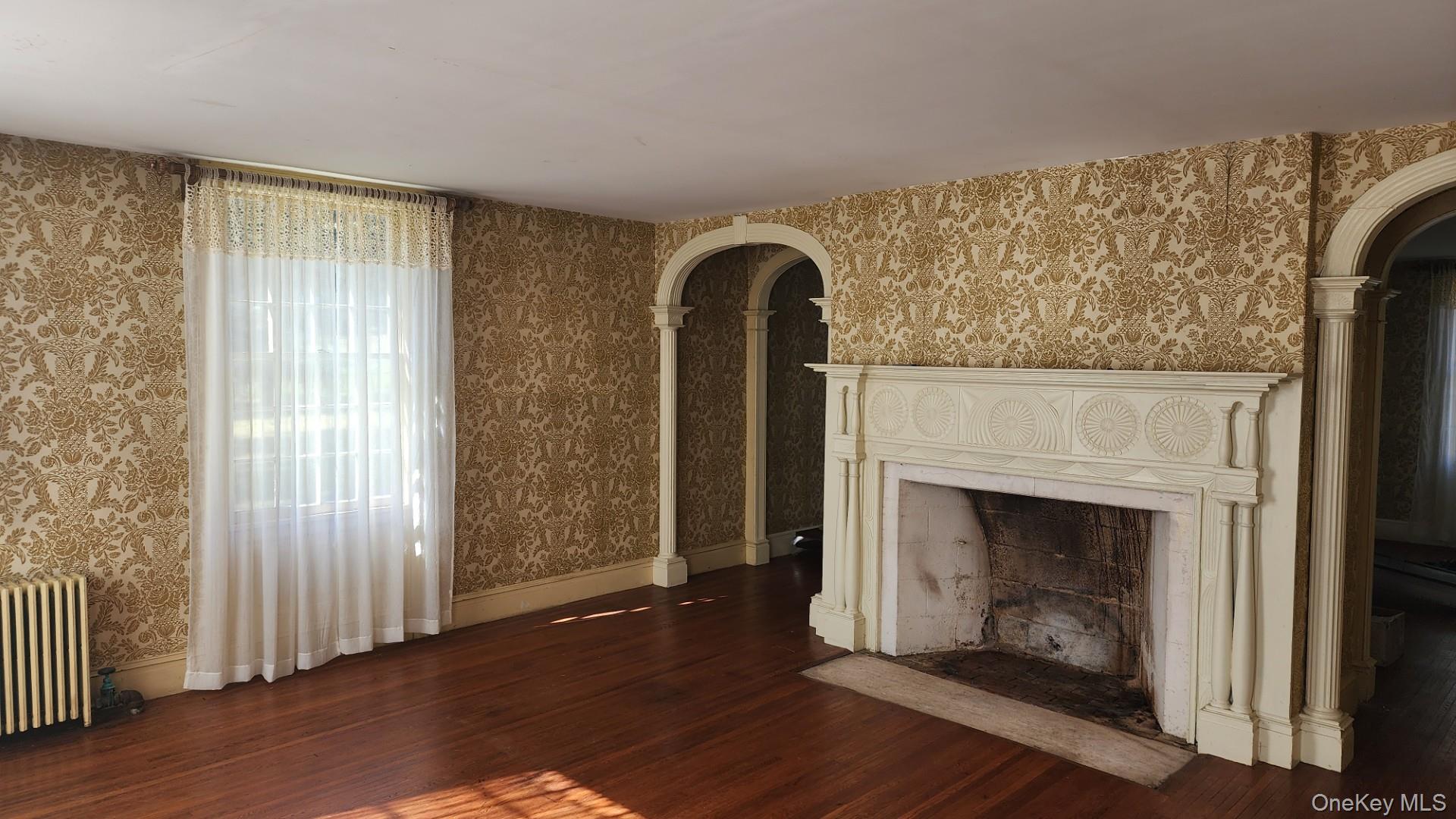 175 Waccabuc Road Goldens Bridge, NY 10526 - Photo 12 of 36 Unfurnished living room with wallpapered walls, dark wood finished floors, a fireplace with flush hearth, radiator heating unit, and arched walkways
