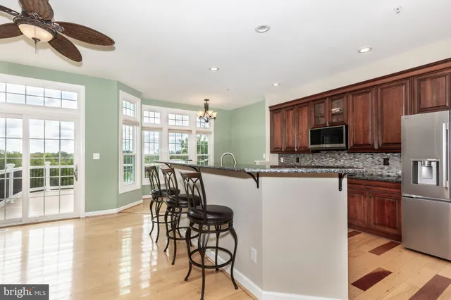 a open kitchen with stainless steel appliances granite countertop a stove top oven a sink a dining table and chairs with wooden floor