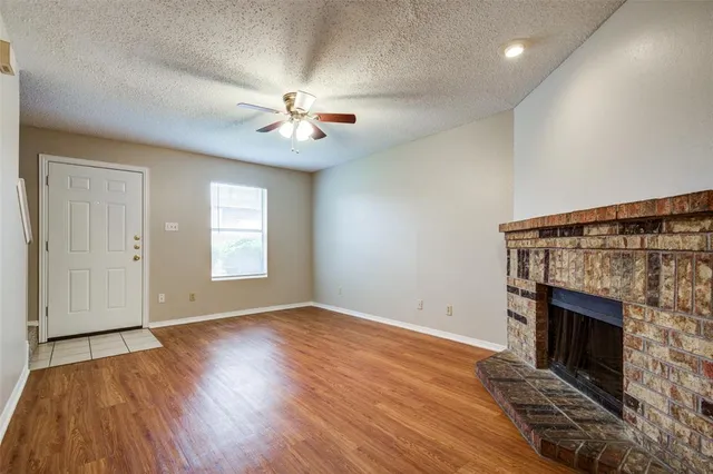 an empty room with windows a fireplace a ceiling fan and wooden floor