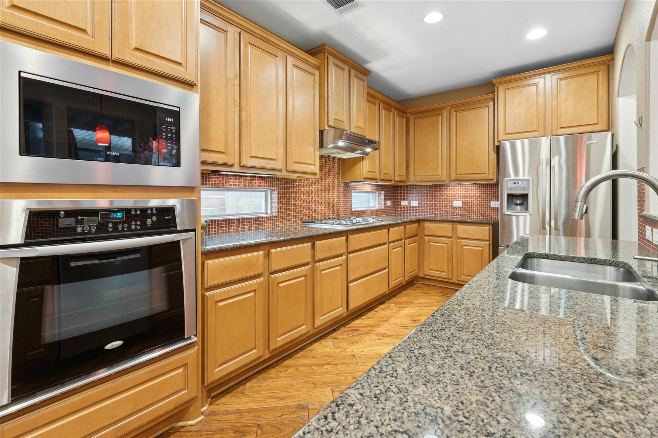 1912 Antone Street Austin, TX 78723 - Photo 8 of 38 Kitchen featuring dark stone countertops, stainless steel appliances, decorative backsplash, light wood-style floors, and recessed lighting