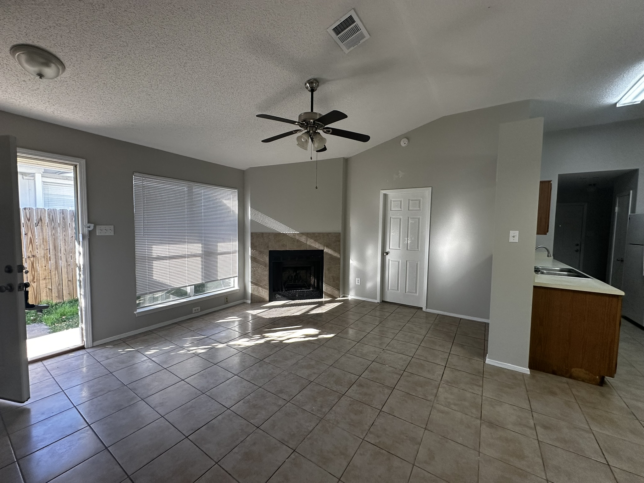2606 Howellwood Way, Unit A Austin, TX 78748 - Photo 3 of 15 Unfurnished living room featuring a textured ceiling, a fireplace, light tile patterned flooring, a ceiling fan, and vaulted ceiling