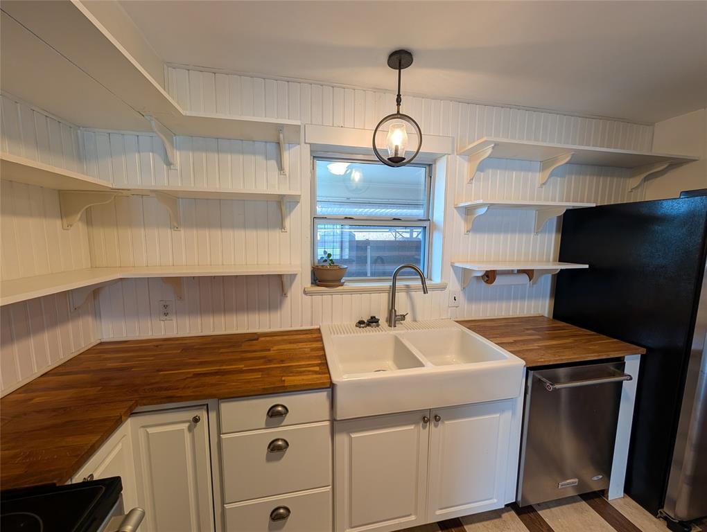 4715 Skillman Street, Unit A Dallas, TX 75206 - Photo 8 of 28 Kitchen featuring white beadboard walls, open shelving, wood-finish countertops, a double farmhouse sink, and a stainless steel dishwasher