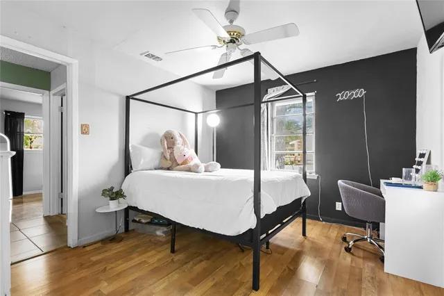 a bedroom with a bed a desk and chair with wooden floor