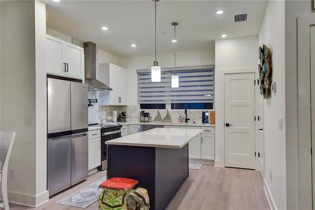 a kitchen with stainless steel appliances kitchen island granite countertop a refrigerator a sink dishwasher a stove and white cabinets with wooden floor