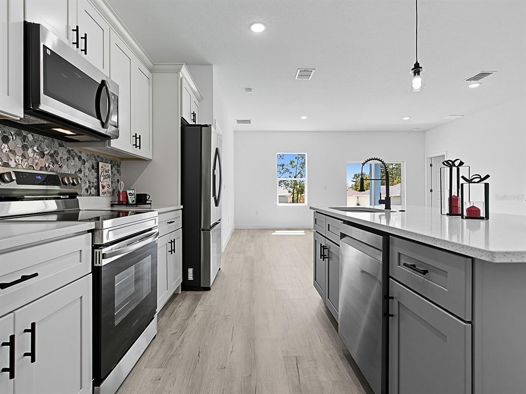 13322 Southwest 85th Circle Ocala, FL 34473 - Photo 4 of 27 a kitchen with stainless steel appliances granite countertop a refrigerator a stove top oven a sink dishwasher and wooden cabinets with wooden floor