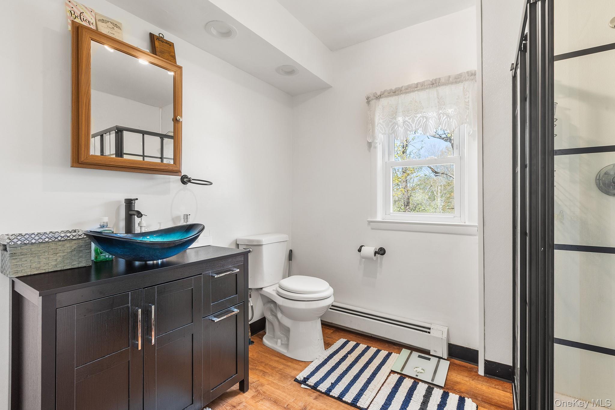 43 Taylor Road Parksville, NY 12768 - Photo 21 of 29 Bathroom featuring a black vanity with a vessel sink, a framed mirror, wood-finish flooring, a window, and a glass-enclosed shower