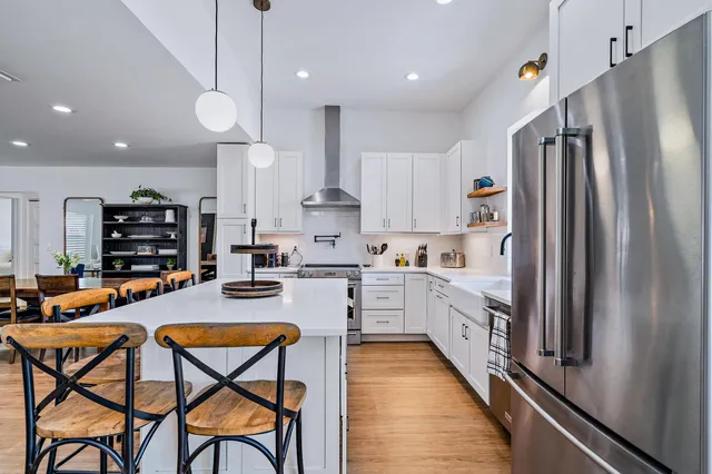 a kitchen with stainless steel appliances granite countertop a refrigerator a sink dishwasher a stove and white cabinets with wooden floor